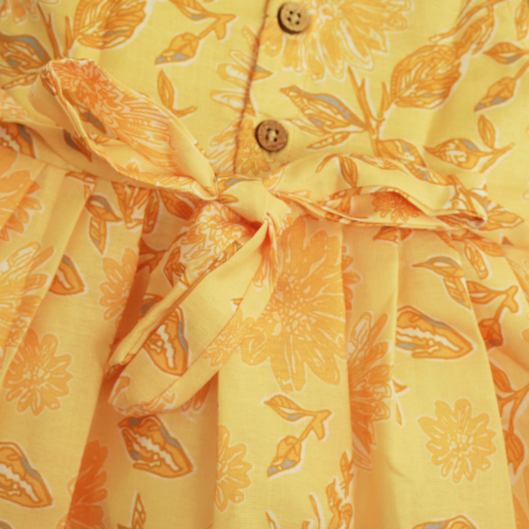 Sunshine yellow sleeveless slub cotton frock for baby girls with all-over orange floral print and pleated skirt, displayed flat on a white fur background with floral basket hanger.