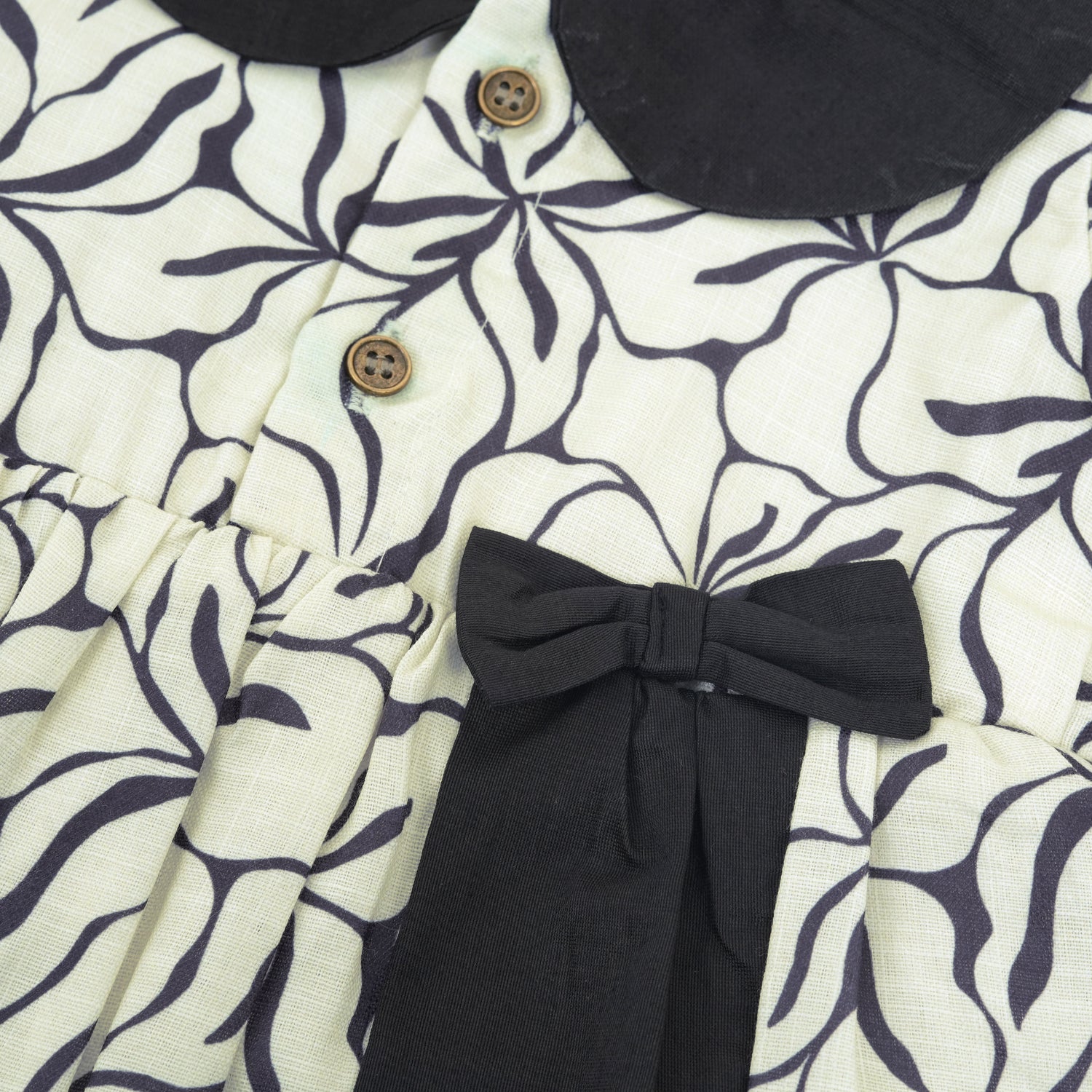 Black & white cotton Side Pleated Frock with floral print, contrast collar & bow detail. Stylish & comfy for baby girls aged 6M–4Y.