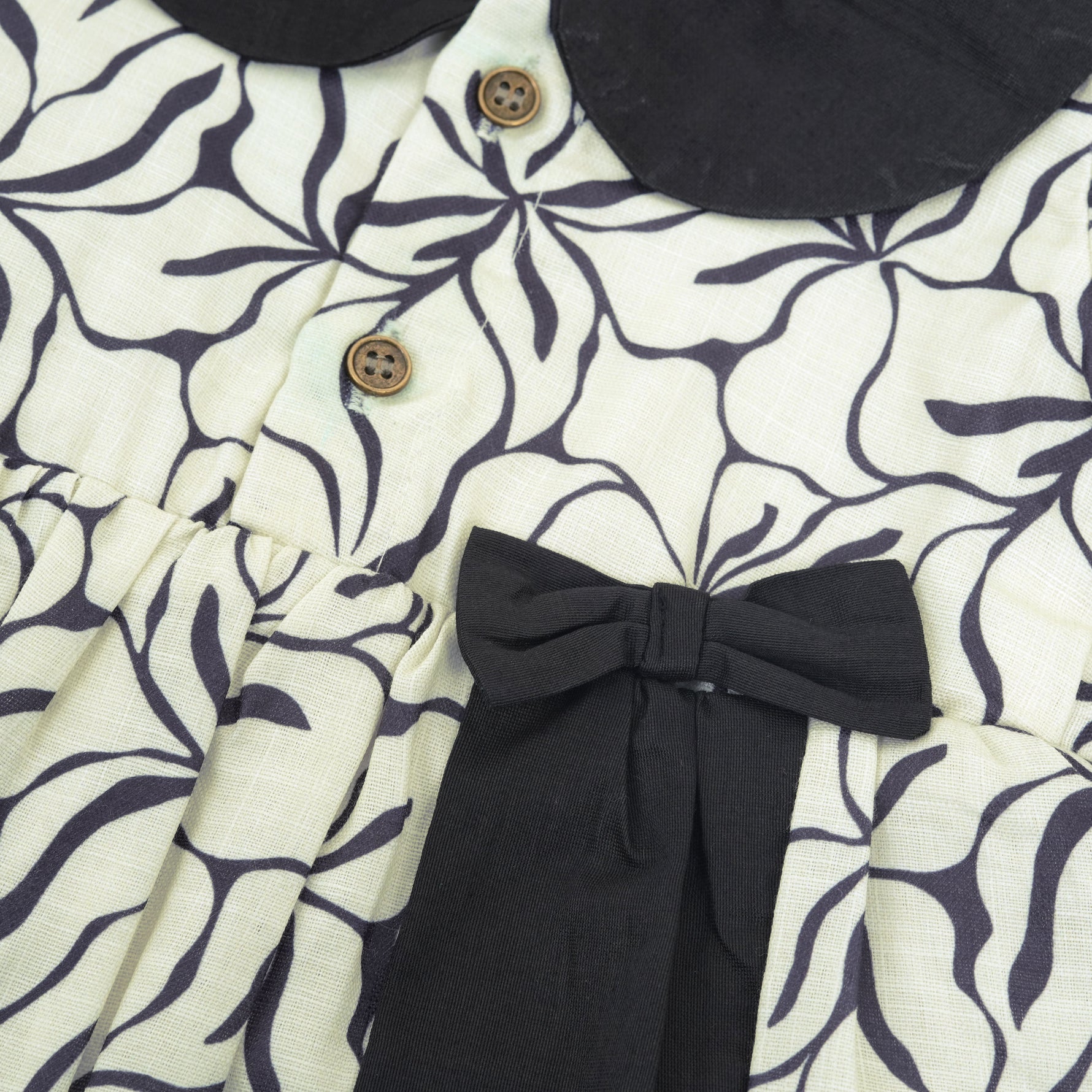 Black & white cotton Side Pleated Frock with floral print, contrast collar & bow detail. Stylish & comfy for baby girls aged 6M–4Y.