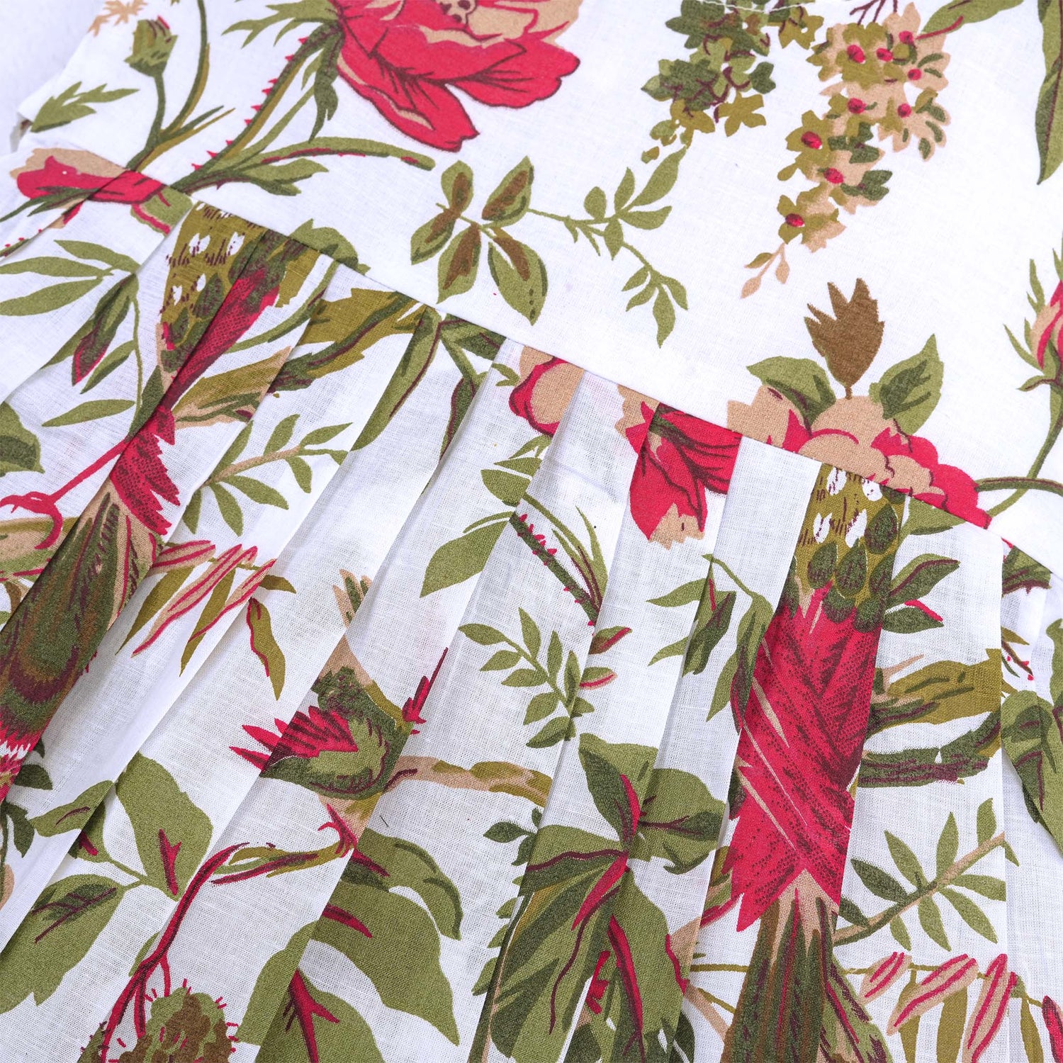 Toddler girl wearing a sleeveless white cotton frock with large pink floral and olive green leaf print – soft summer dress from Boon Babies, Coimbatore.