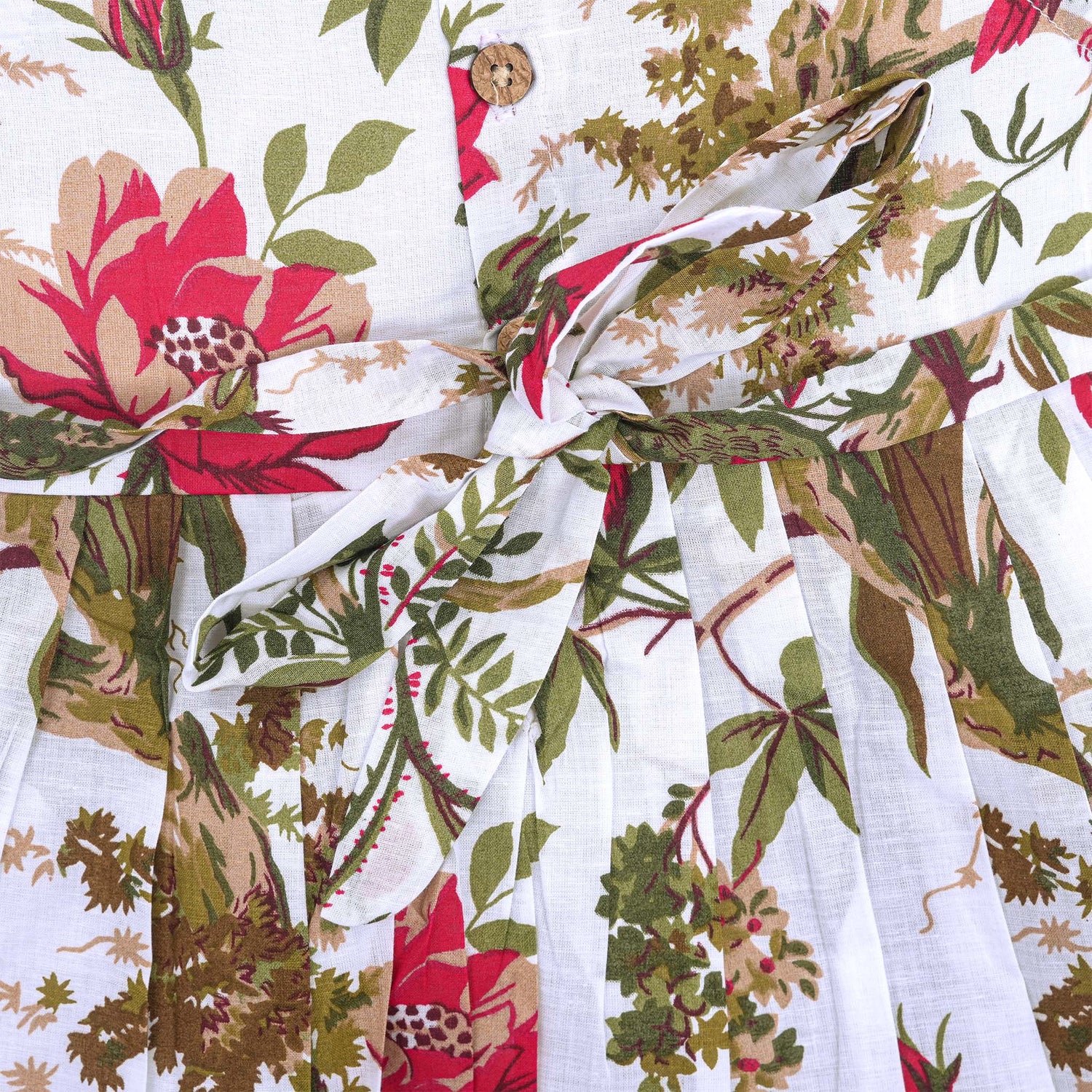 Toddler girl wearing a sleeveless white cotton frock with large pink floral and olive green leaf print – soft summer dress from Boon Babies, Coimbatore.