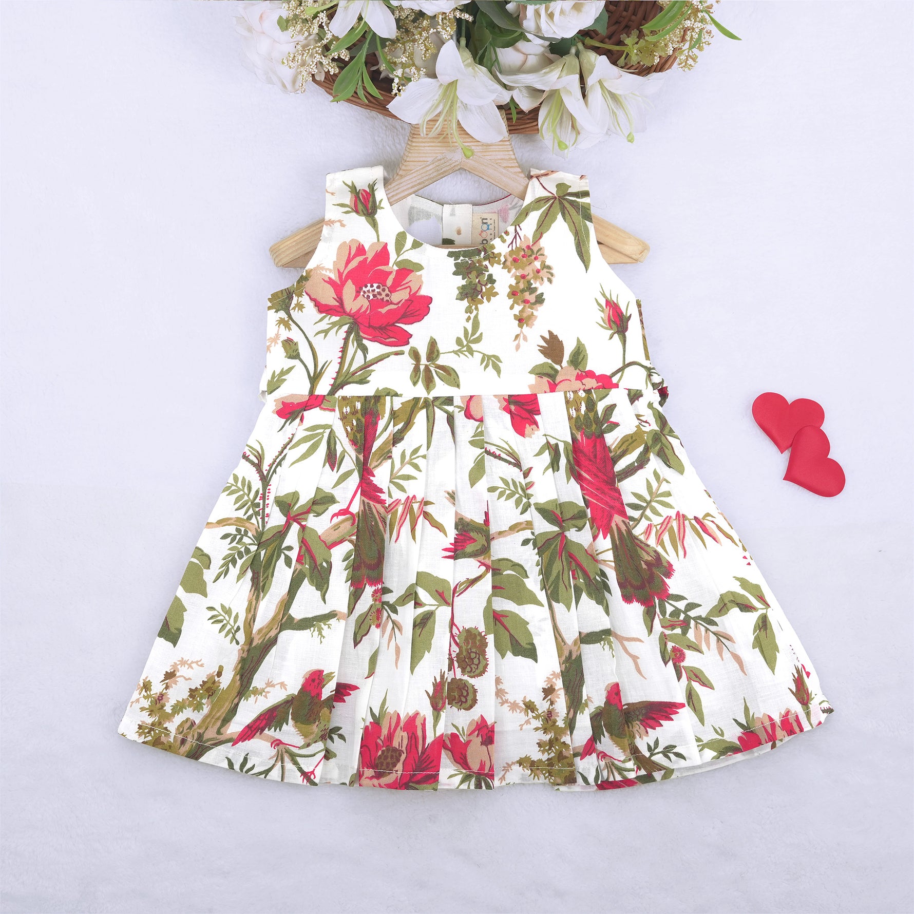 Toddler girl wearing a sleeveless white cotton frock with large pink floral and olive green leaf print – soft summer dress from Boon Babies, Coimbatore.