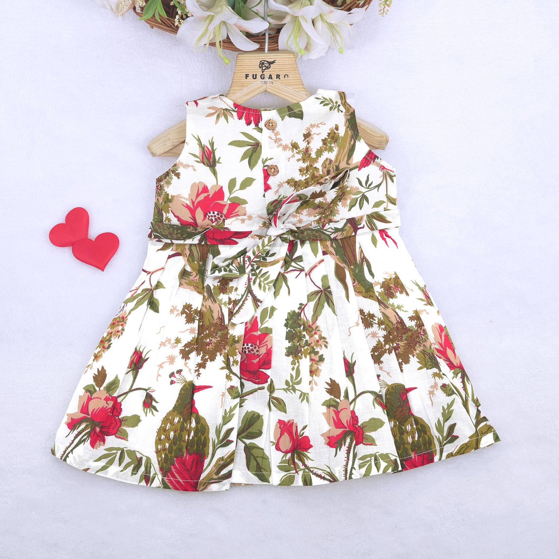 Toddler girl wearing a sleeveless white cotton frock with large pink floral and olive green leaf print – soft summer dress from Boon Babies, Coimbatore.