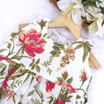 Toddler girl wearing a sleeveless white cotton frock with large pink floral and olive green leaf print – soft summer dress from Boon Babies, Coimbatore.