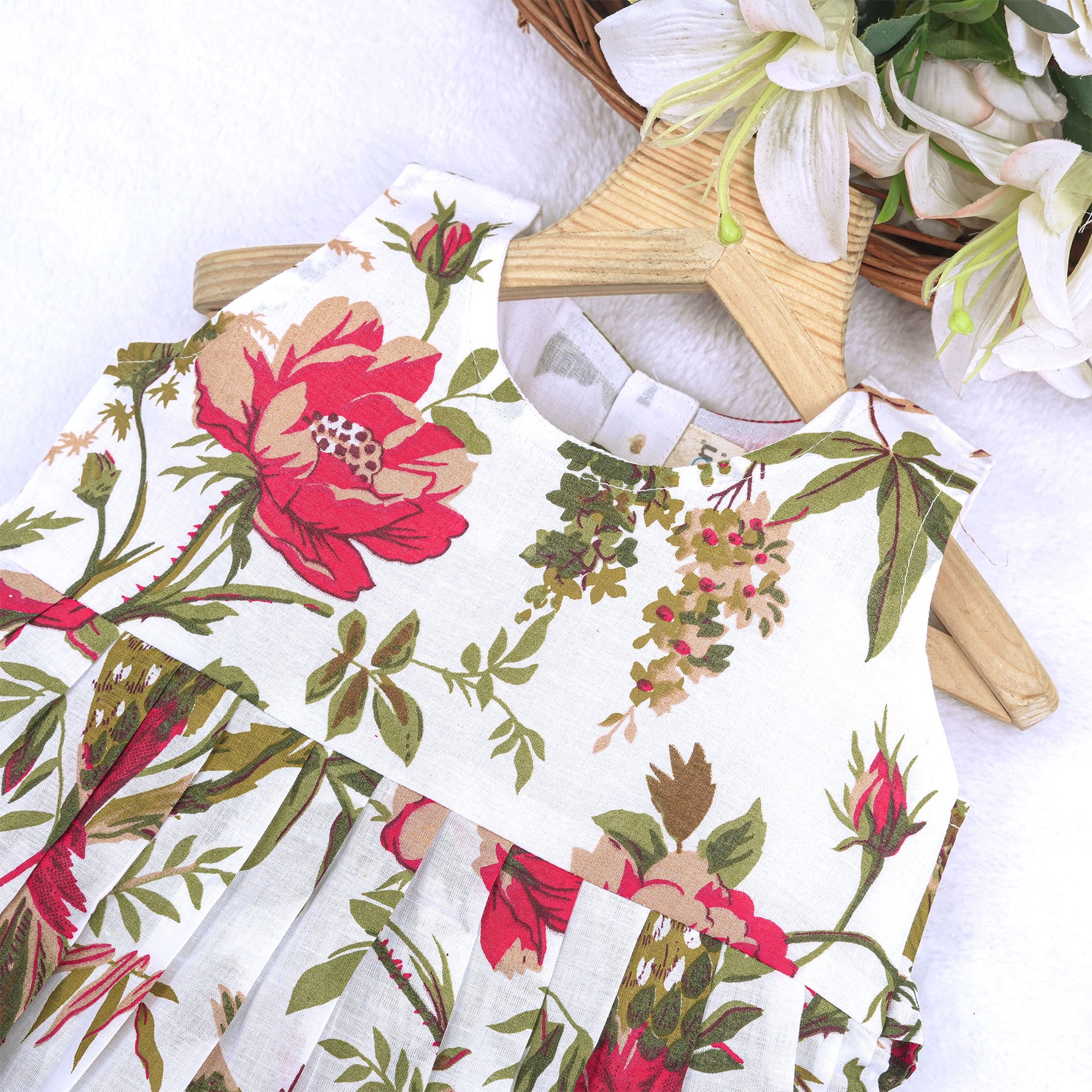 Toddler girl wearing a sleeveless white cotton frock with large pink floral and olive green leaf print – soft summer dress from Boon Babies, Coimbatore.