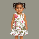 Toddler girl wearing a sleeveless white cotton frock with large pink floral and olive green leaf print – soft summer dress from Boon Babies, Coimbatore.
