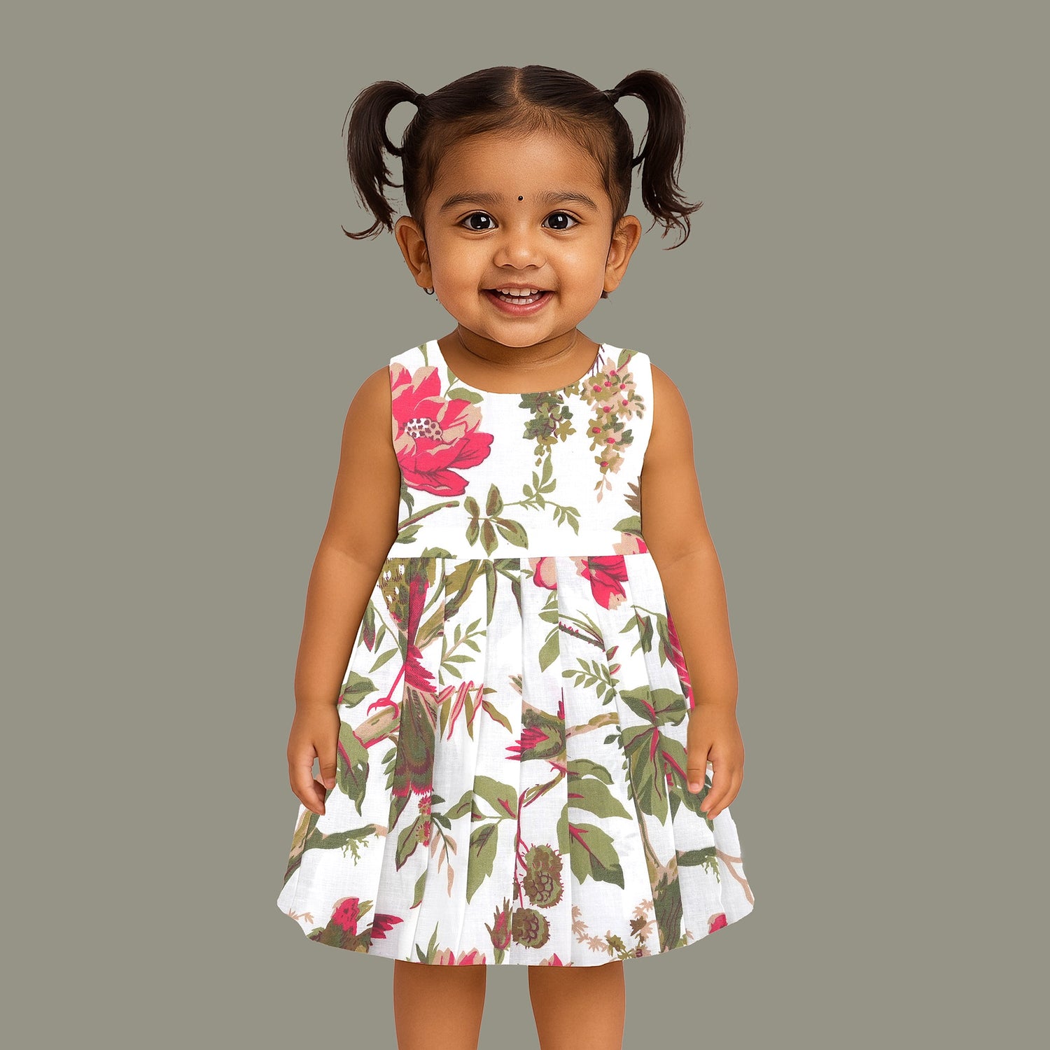 Toddler girl wearing a sleeveless white cotton frock with large pink floral and olive green leaf print – soft summer dress from Boon Babies, Coimbatore.