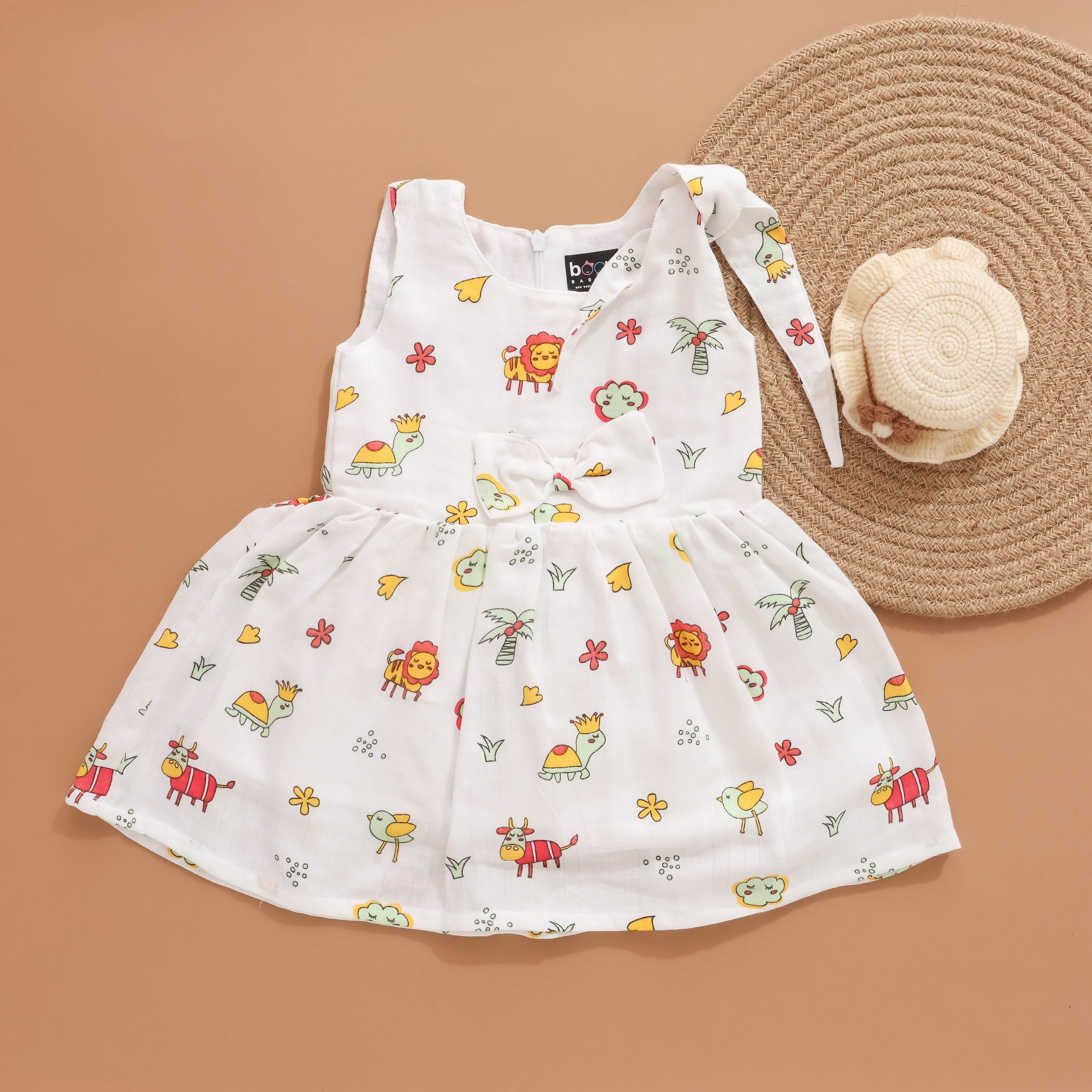 Baby girl wearing Boon Babies printed muslin knot frock with bow detail, 6-12 months, featuring colorful animal print and layered fabric.