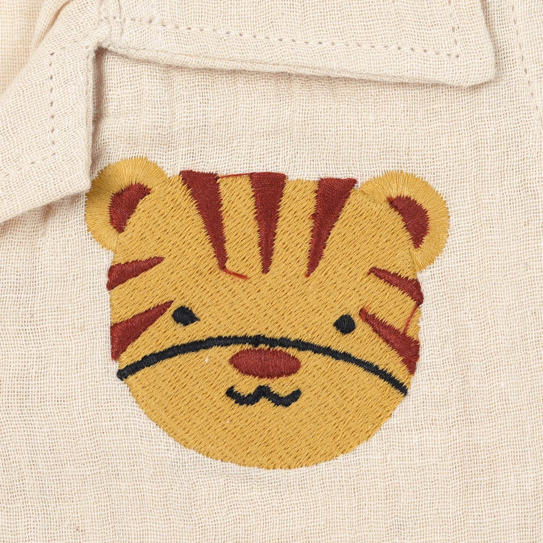 Cream crinkle muslin shirt and shorts set for boys featuring tiger face embroidery, open collar, and elastic shorts – from Boon Babies, Coimbatore.
