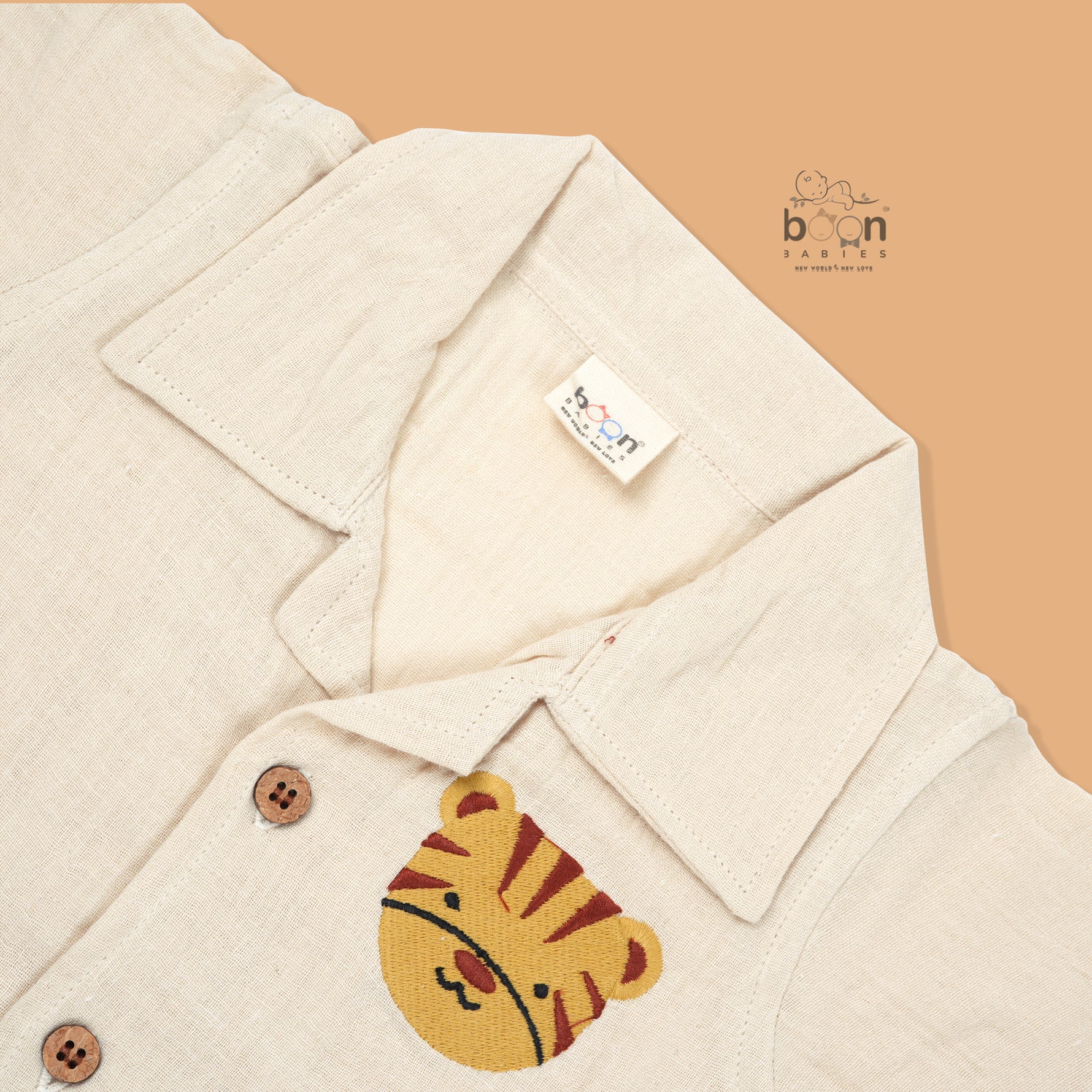 Cream crinkle muslin shirt and shorts set for boys featuring tiger face embroidery, open collar, and elastic shorts – from Boon Babies, Coimbatore.
