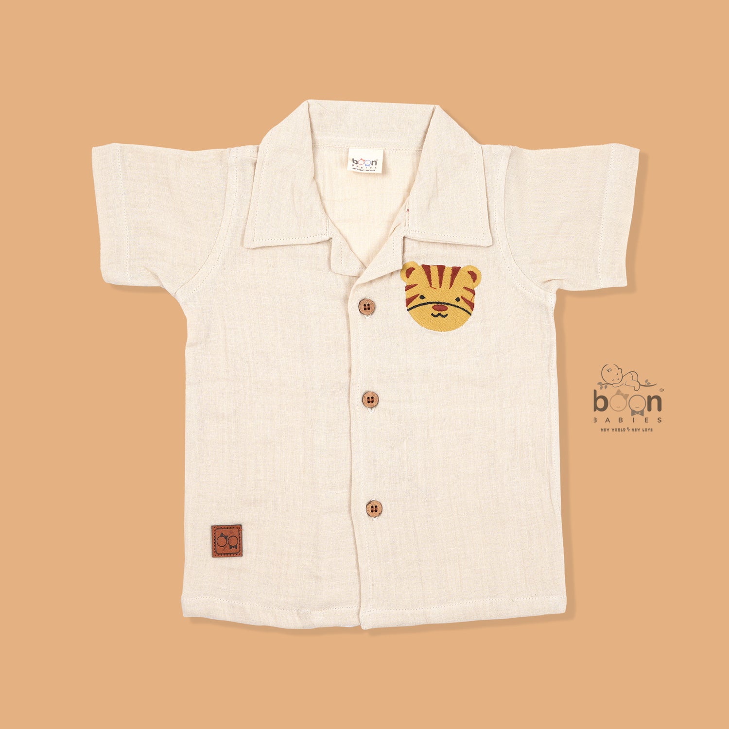 Cream crinkle muslin shirt and shorts set for boys featuring tiger face embroidery, open collar, and elastic shorts – from Boon Babies, Coimbatore.

