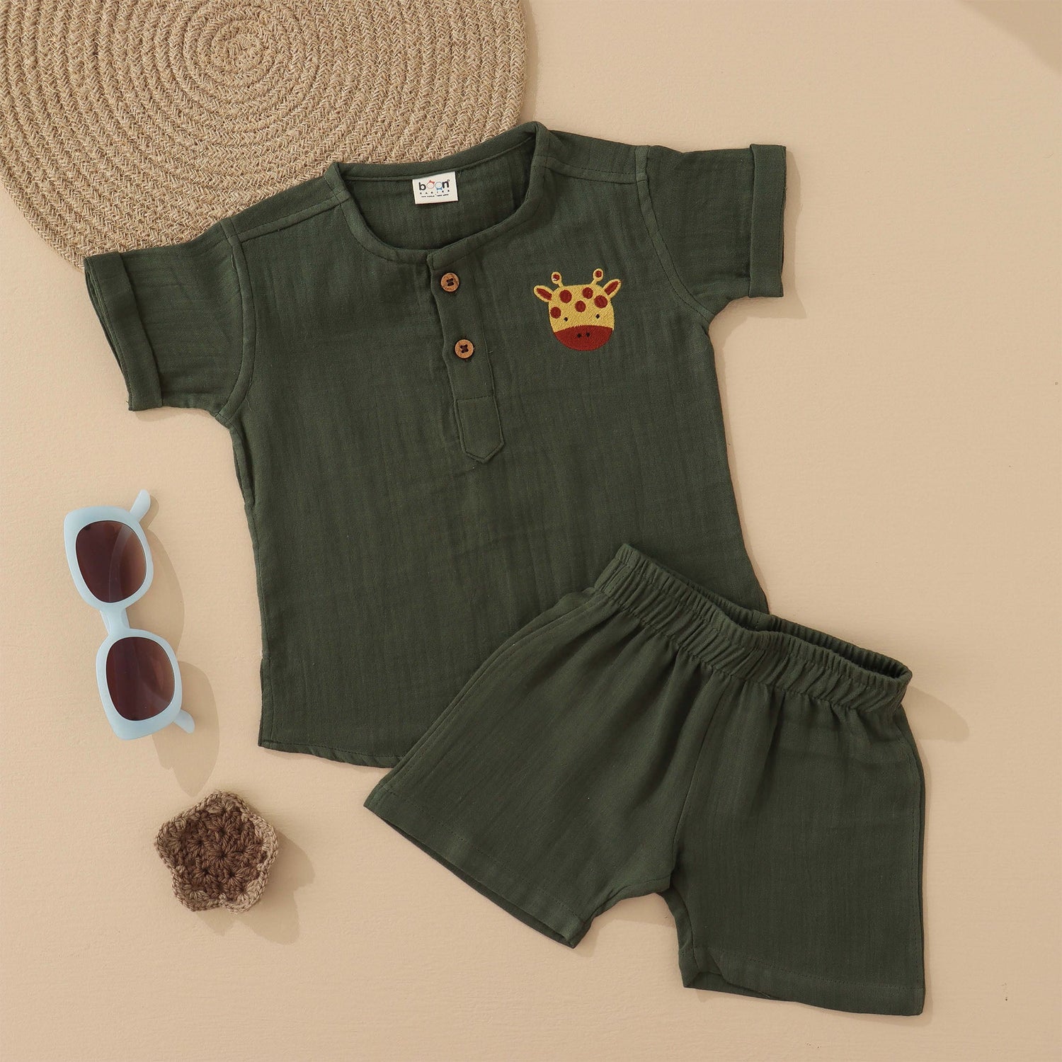 Dark olive green boys muslin co-ord with giraffe patch embroidery, round neck shirt with buttons, and elastic shorts – by Boon Babies, Coimbatore.
