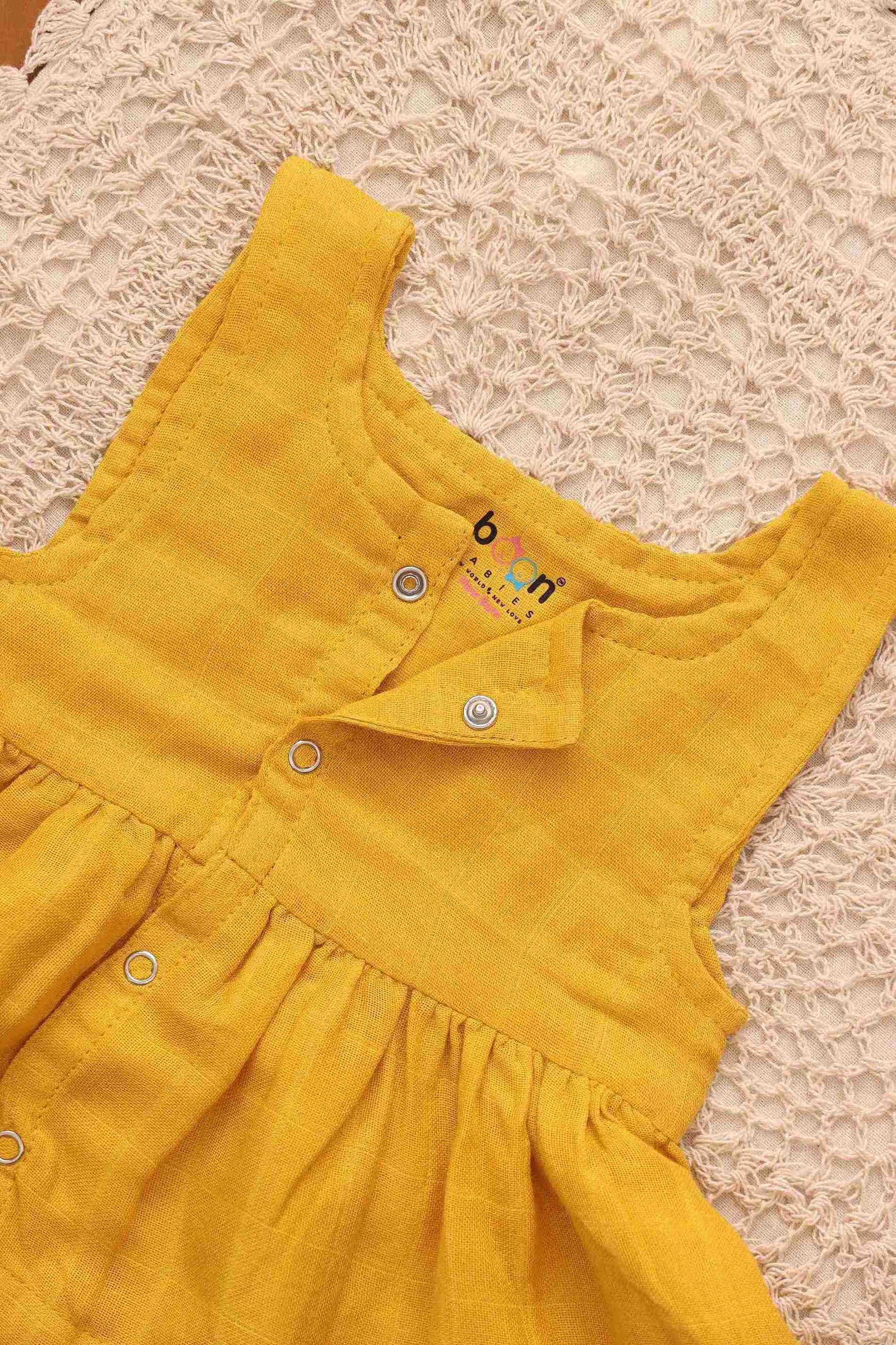 Baby girl wearing a yellow sleeveless solid muslin frock by Boon Babies, featuring four layers for a playful, elegant look.