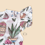 Cotton baby romper with colorful botanical and bird print, flutter sleeves, side bows, and front snap buttons – from Boon Babies, Coimbatore.
