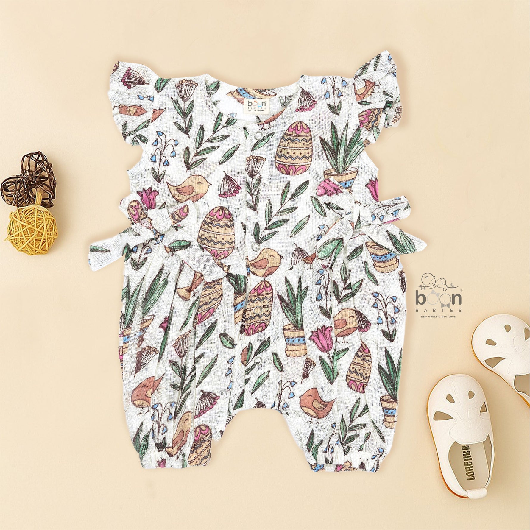 Cotton baby romper with colorful botanical and bird print, flutter sleeves, side bows, and front snap buttons – from Boon Babies, Coimbatore.
