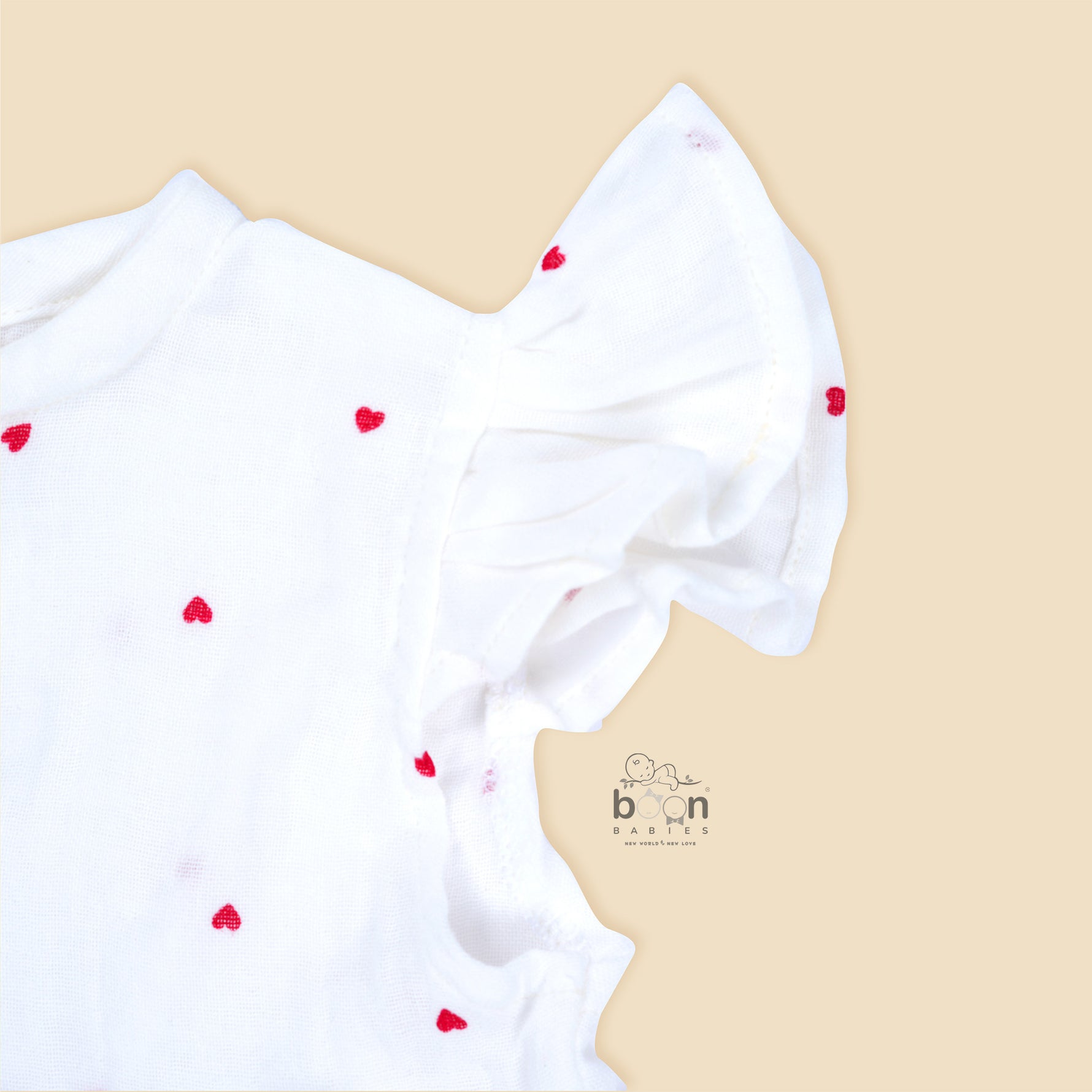 White muslin baby romper with tiny red heart prints, featuring frill sleeves, side bows, and front snap buttons – from Boon Babies, Coimbatore.
