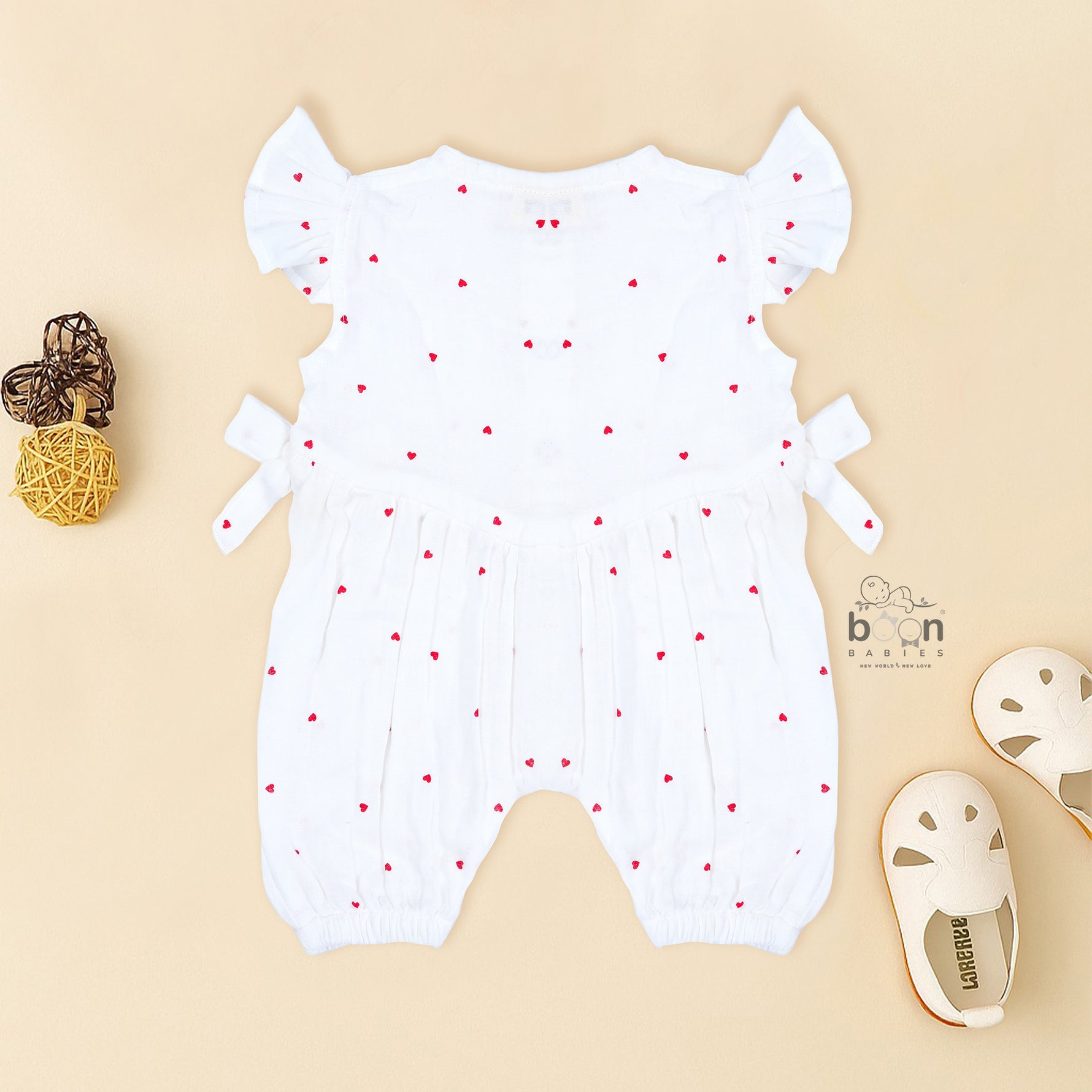 White muslin baby romper with tiny red heart prints, featuring frill sleeves, side bows, and front snap buttons – from Boon Babies, Coimbatore.