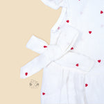 White muslin baby romper with tiny red heart prints, featuring frill sleeves, side bows, and front snap buttons – from Boon Babies, Coimbatore.
