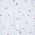 White muslin baby romper with tiny red heart prints, featuring frill sleeves, side bows, and front snap buttons – from Boon Babies, Coimbatore.