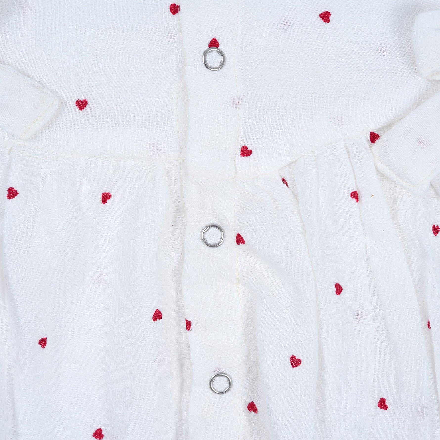 White muslin baby romper with tiny red heart prints, featuring frill sleeves, side bows, and front snap buttons – from Boon Babies, Coimbatore.