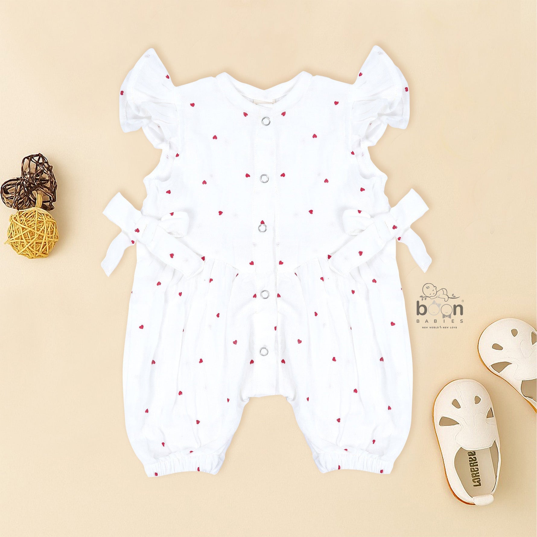 White muslin baby romper with tiny red heart prints, featuring frill sleeves, side bows, and front snap buttons – from Boon Babies, Coimbatore.