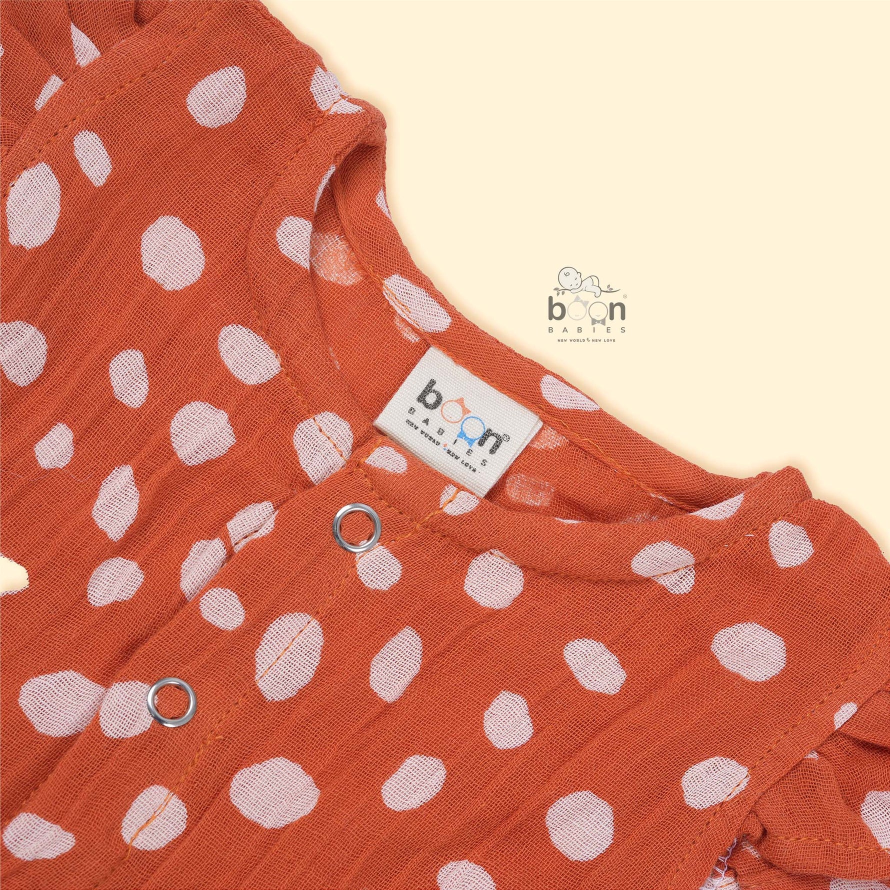 Rust orange baby romper with white polka dots, flutter sleeves, and side bows – made from soft crinkled muslin for babies aged 0–12 months by Boon Babies, Coimbatore.