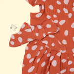 Rust orange baby romper with white polka dots, flutter sleeves, and side bows – made from soft crinkled muslin for babies aged 0–12 months by Boon Babies, Coimbatore.Rust orange baby romper with white polka dots, flutter sleeves, and side bows – made from soft crinkled muslin for babies aged 0–12 months by Boon Babies, Coimbatore.