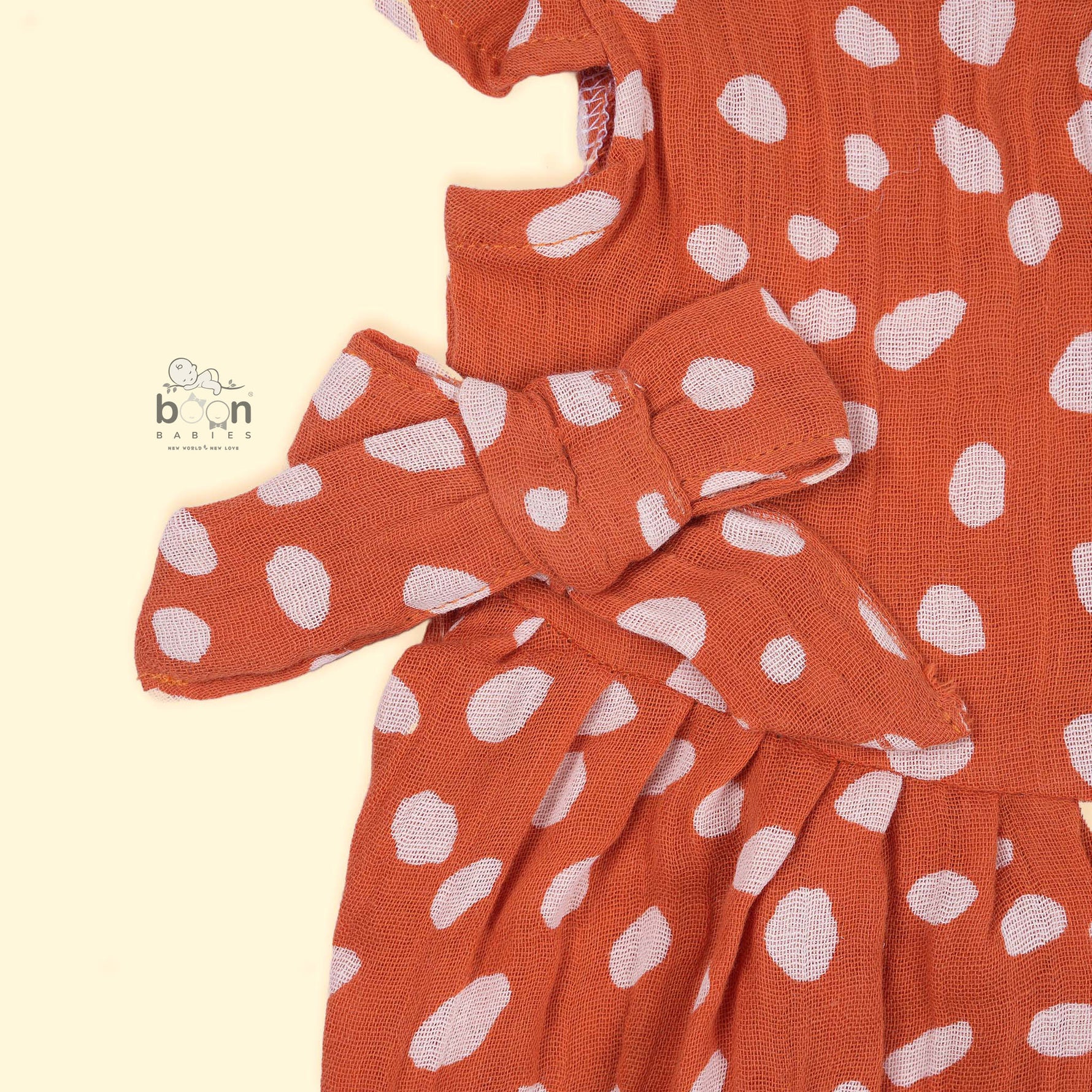 Rust orange baby romper with white polka dots, flutter sleeves, and side bows – made from soft crinkled muslin for babies aged 0–12 months by Boon Babies, Coimbatore.Rust orange baby romper with white polka dots, flutter sleeves, and side bows – made from soft crinkled muslin for babies aged 0–12 months by Boon Babies, Coimbatore.