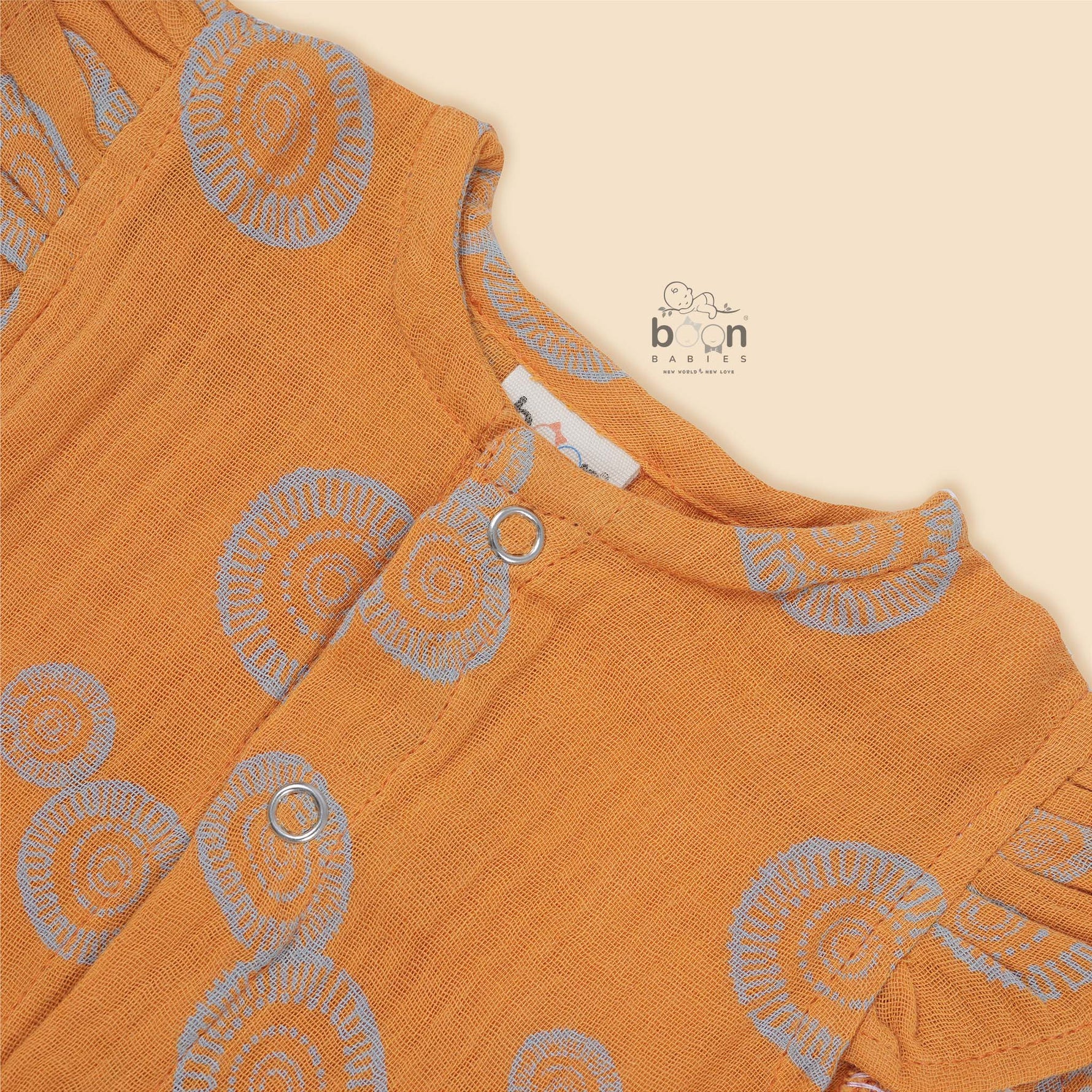 Crinkled muslin baby romper in rust orange with spiral print, flutter sleeves, and snap-down front – soft summer outfit for babies from Boon Babies, Coimbatore.