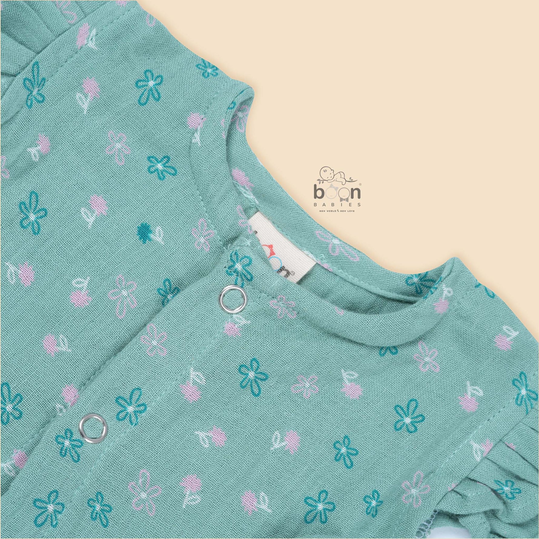 Teal blue baby romper with white floral prints, flutter sleeves, and side bows made from breathable crinkled muslin – designed for babies aged 0–12 months by Boon Babies, Coimbatore.