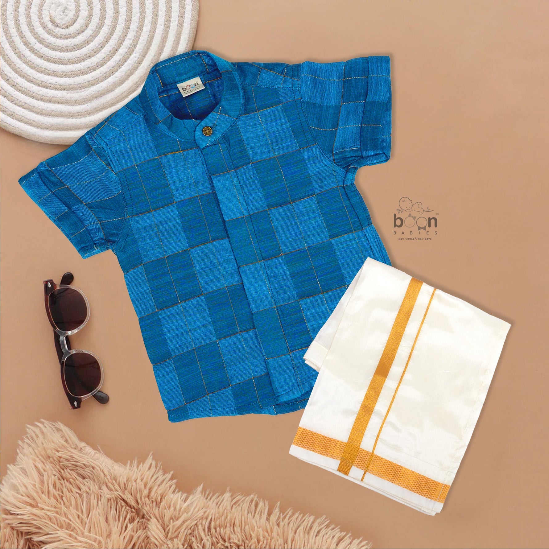 Blue checked silk shirt with Chinese collar and white dhoti with gold border – boys traditional outfit from Boon Babies, styled flatlay.
