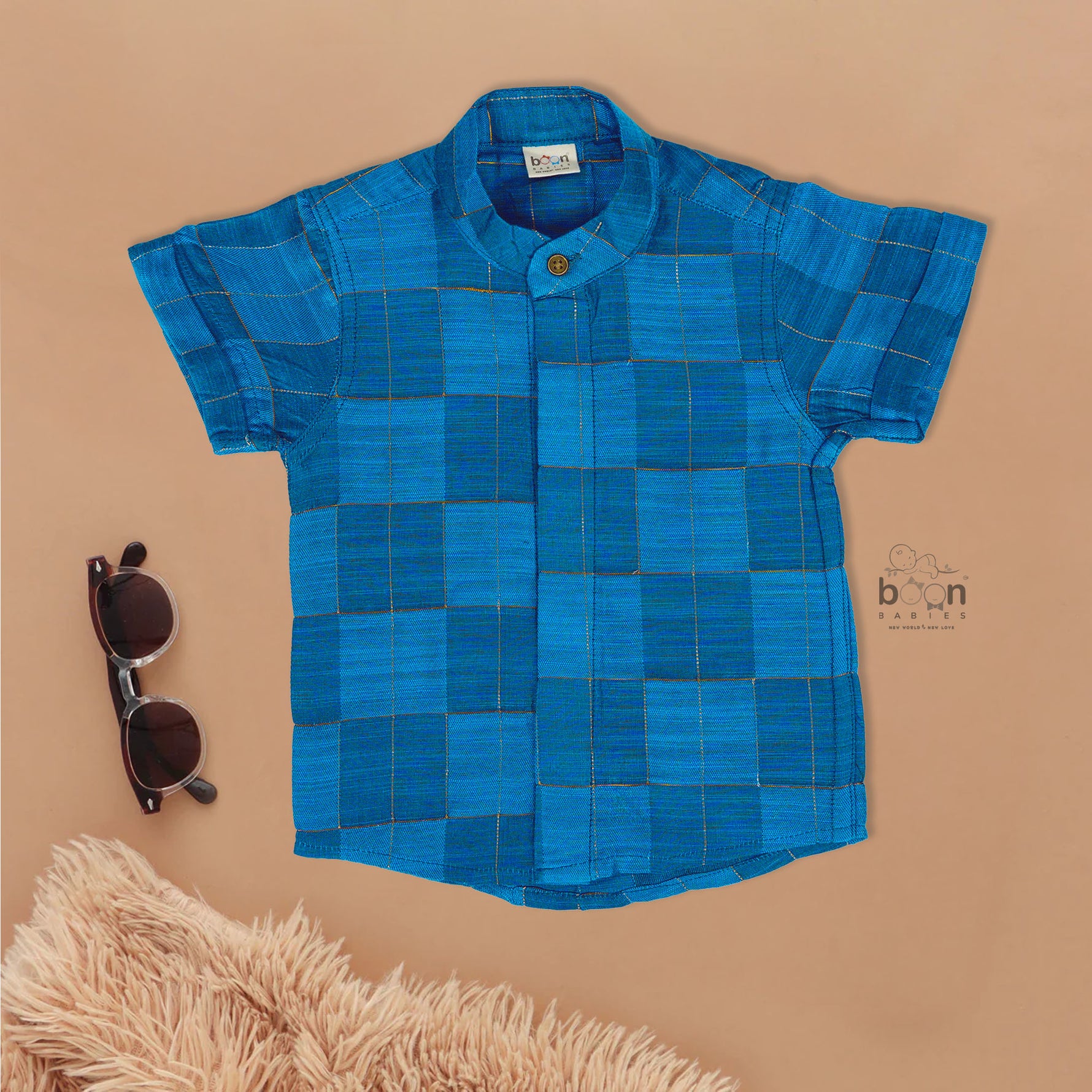 Blue checked silk shirt with Chinese collar and white dhoti with gold border – boys traditional outfit from Boon Babies, styled flatlay.

