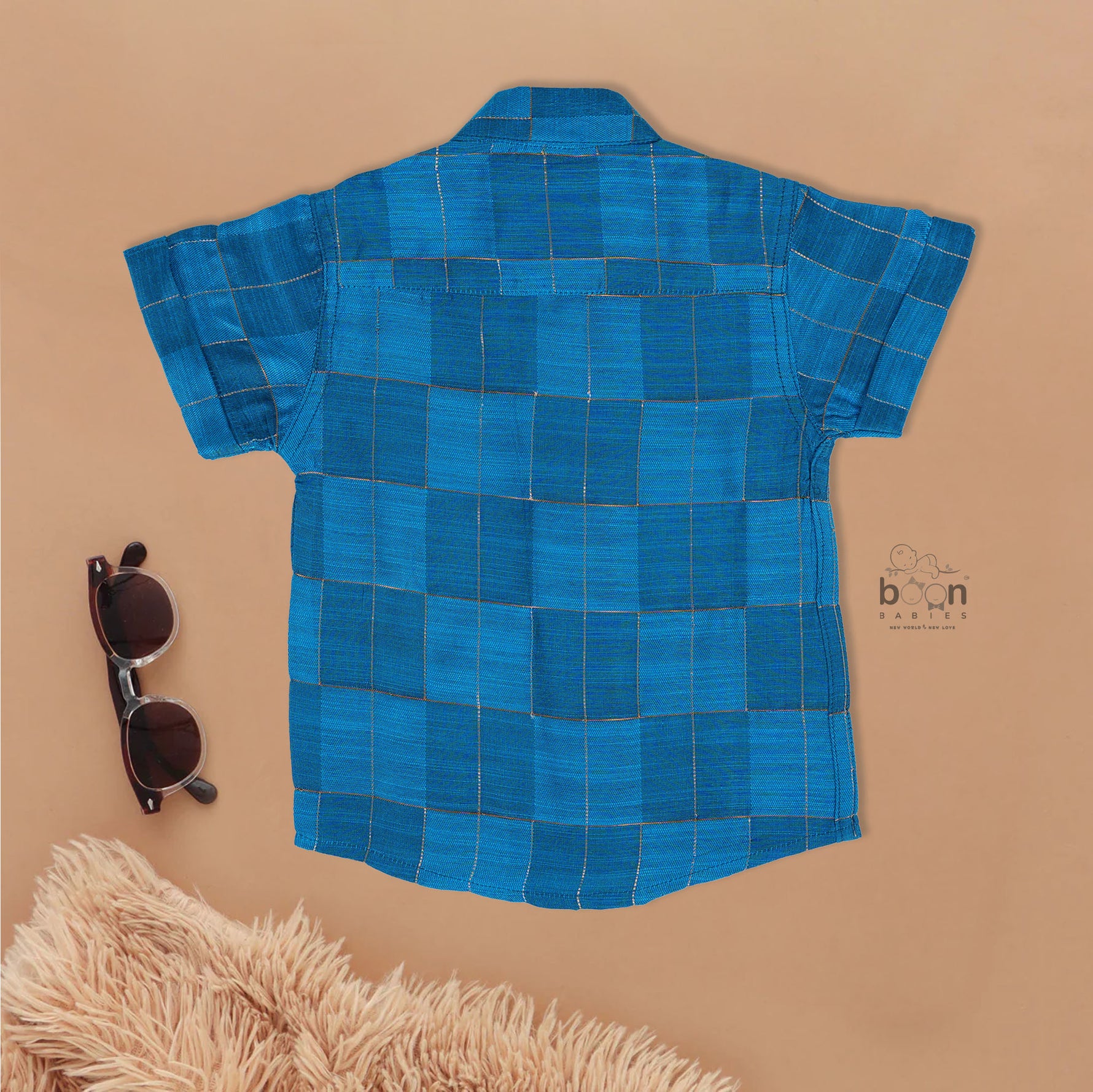 Blue checked silk shirt with Chinese collar and white dhoti with gold border – boys traditional outfit from Boon Babies, styled flatlay.
