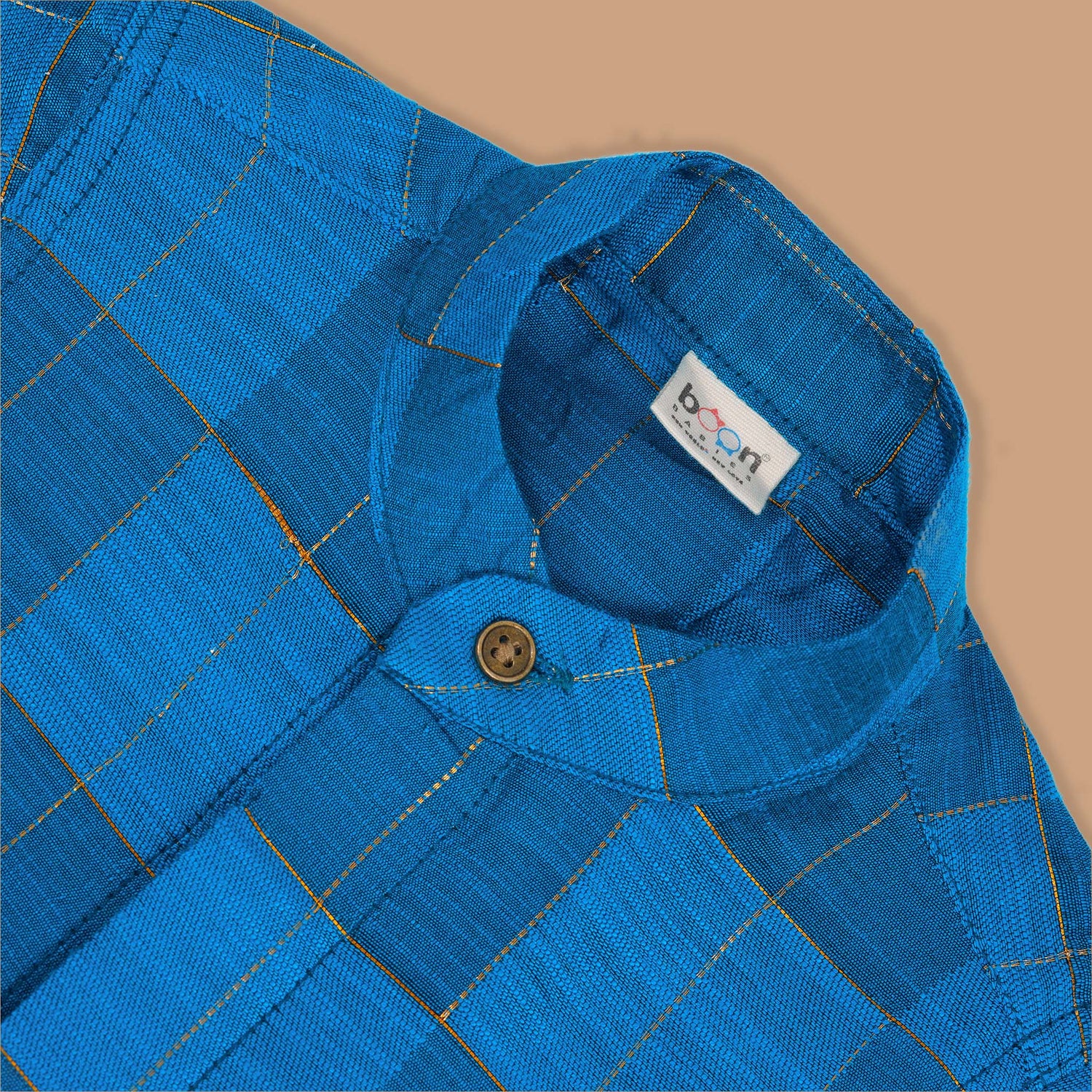 Blue checked silk shirt with Chinese collar and white dhoti with gold border – boys traditional outfit from Boon Babies, styled flatlay.
