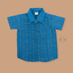 Boys festive outfit featuring a royal blue checked silk shirt and white dhoti with gold border – traditional South Indian attire by Boon Babies.
