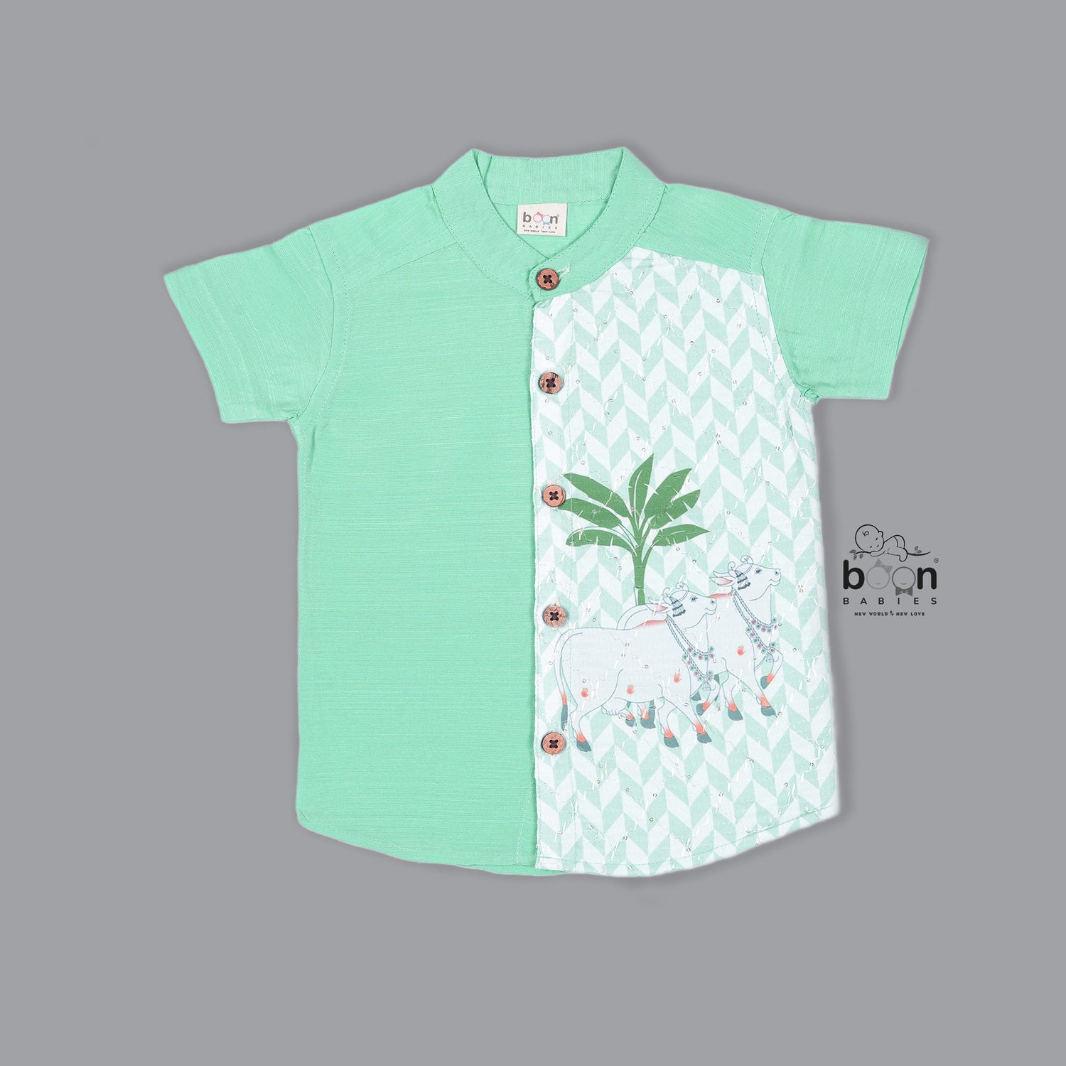 Boys’ mint green silk shirt with illustrated cow and palm tree print panel, paired with a cream silk pattu dhoti with golden border – Boon Babies ethnic set for toddlers.