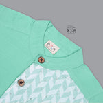 Boys’ mint green silk shirt with illustrated cow and palm tree print panel, paired with a cream silk pattu dhoti with golden border – Boon Babies ethnic set for toddlers.