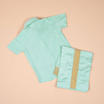 Teal blue silk dhoti shirt set for baby boys featuring a wooden-button shirt and gold-bordered dhoti, displayed flat on a beige background with floral props.