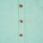 Teal blue silk dhoti shirt set for baby boys featuring a wooden-button shirt and gold-bordered dhoti, displayed flat on a beige background with floral props.