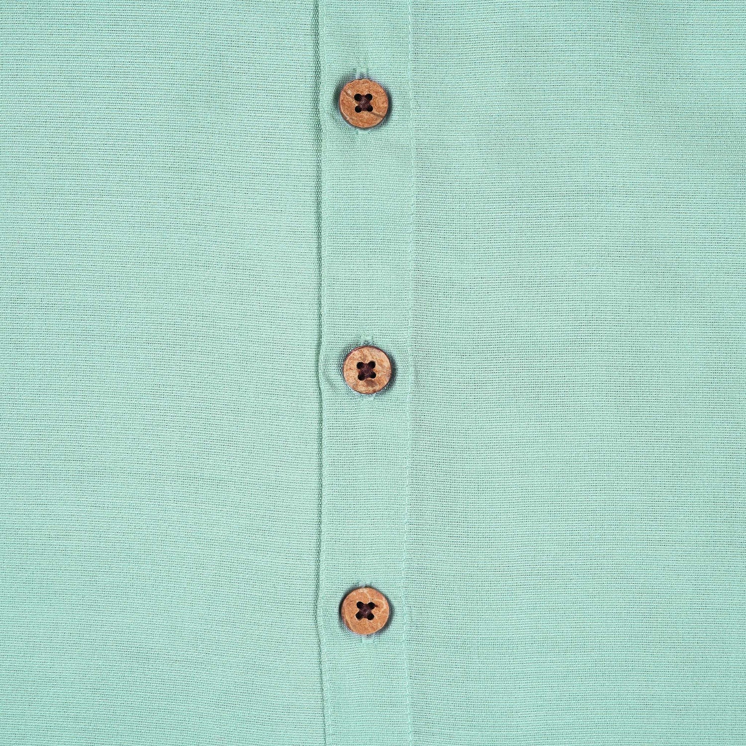 Teal blue silk dhoti shirt set for baby boys featuring a wooden-button shirt and gold-bordered dhoti, displayed flat on a beige background with floral props.