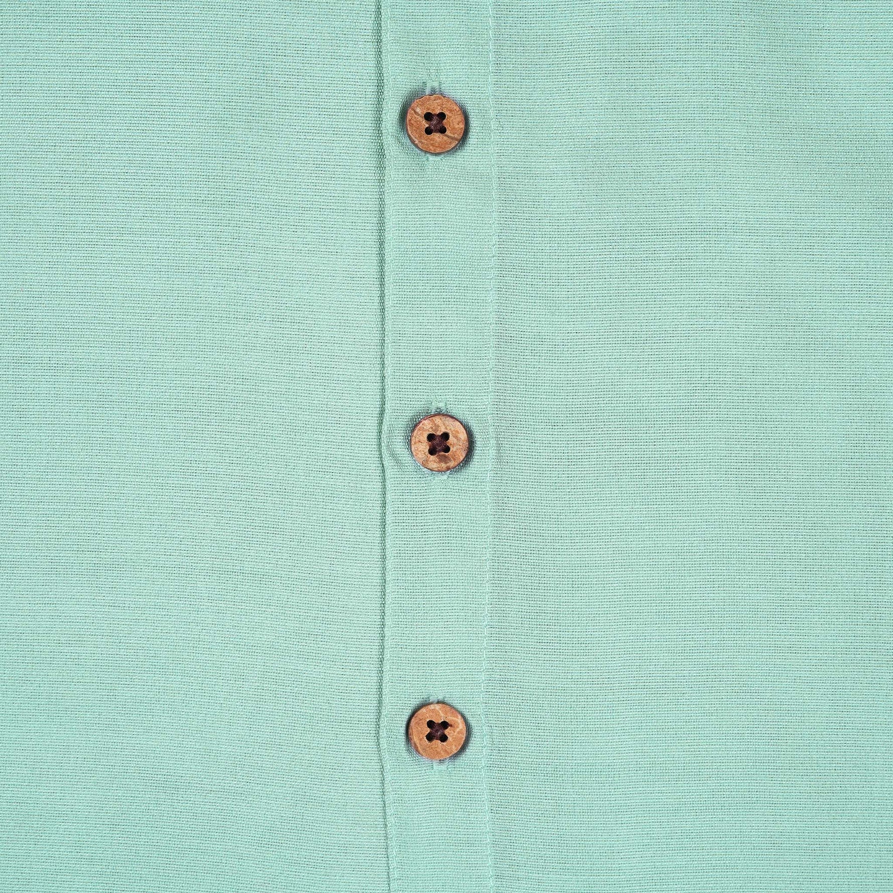 Teal blue silk dhoti shirt set for baby boys featuring a wooden-button shirt and gold-bordered dhoti, displayed flat on a beige background with floral props.