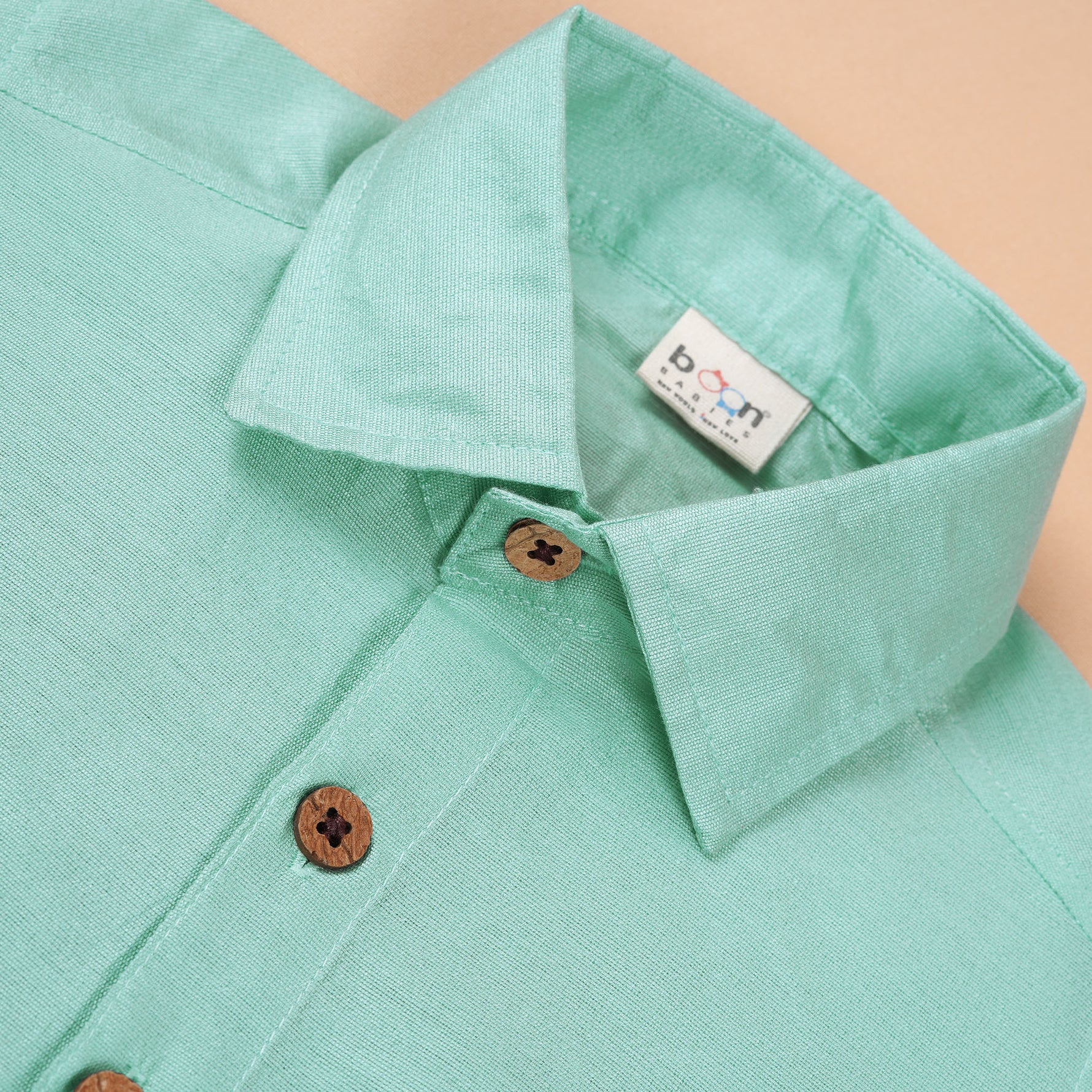 Teal blue silk dhoti shirt set for baby boys featuring a wooden-button shirt and gold-bordered dhoti, displayed flat on a beige background with floral props.